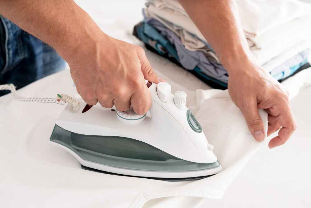 Pose d'une étiquette thermocollante sur un vêtement avec plan serré sur les mains en train de repasser pour fixer l'étiquette